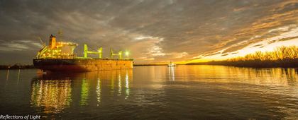 Cargo ship beneath a gold sunrise with light trails along the water