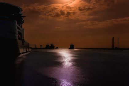 Copper moonlight reflected across a quiet industrial harbor
