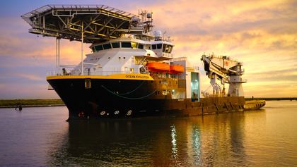 Offshore work vessel reflected in golden water at sunset
