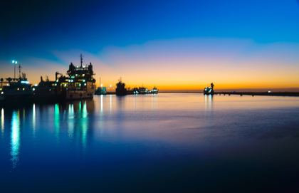 Blue-hour harbor panorama with ships and lights reflected across calm water