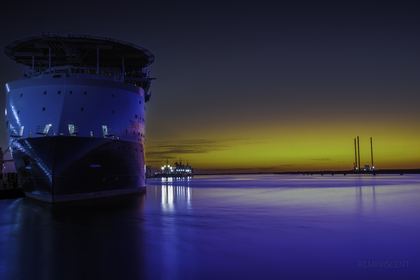 The bow of a large ship against green and violet light at dusk