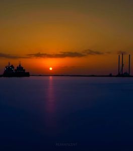 Orange sun near the horizon over deep blue water