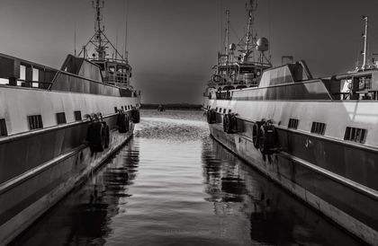Black-and-white view down the water corridor between two workboats