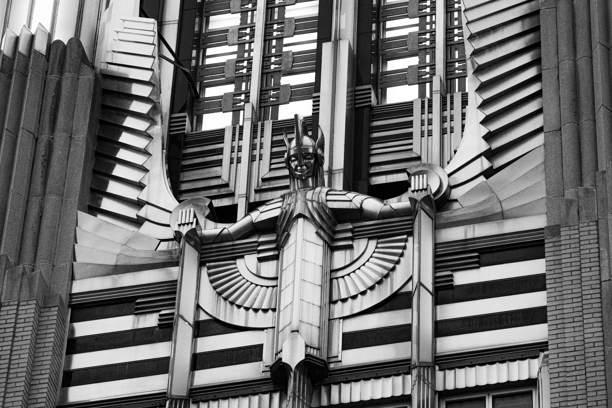 Angled black-and-white view of a sculpted figure surrounded by radiating Art Deco ornament