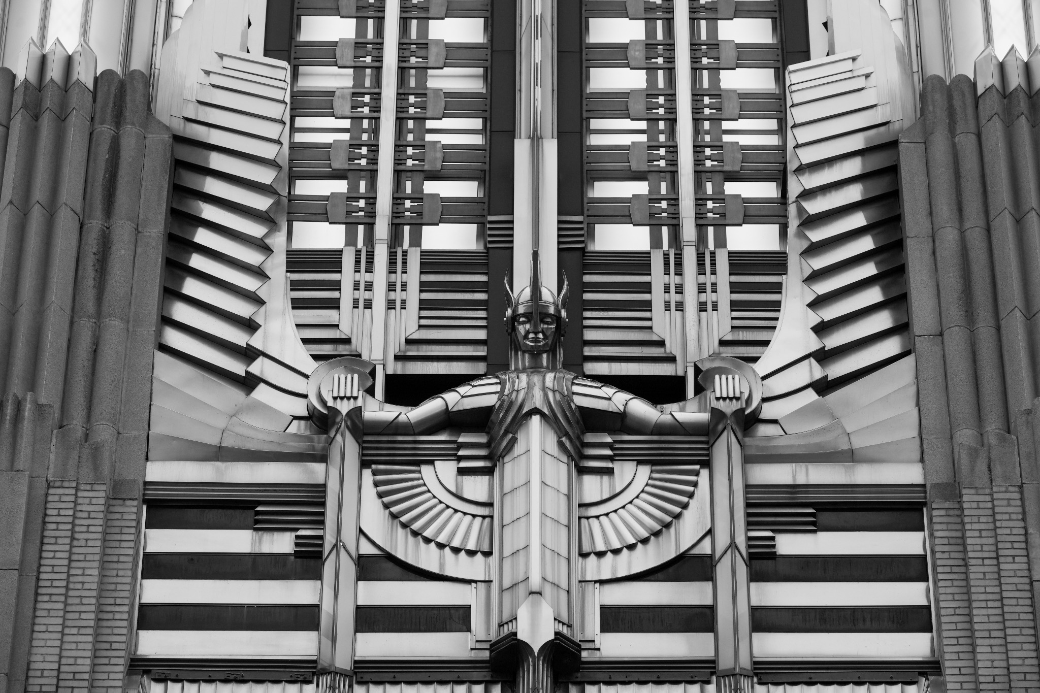 Centered black-and-white architectural figure with outstretched arms and symmetrical Art Deco details
