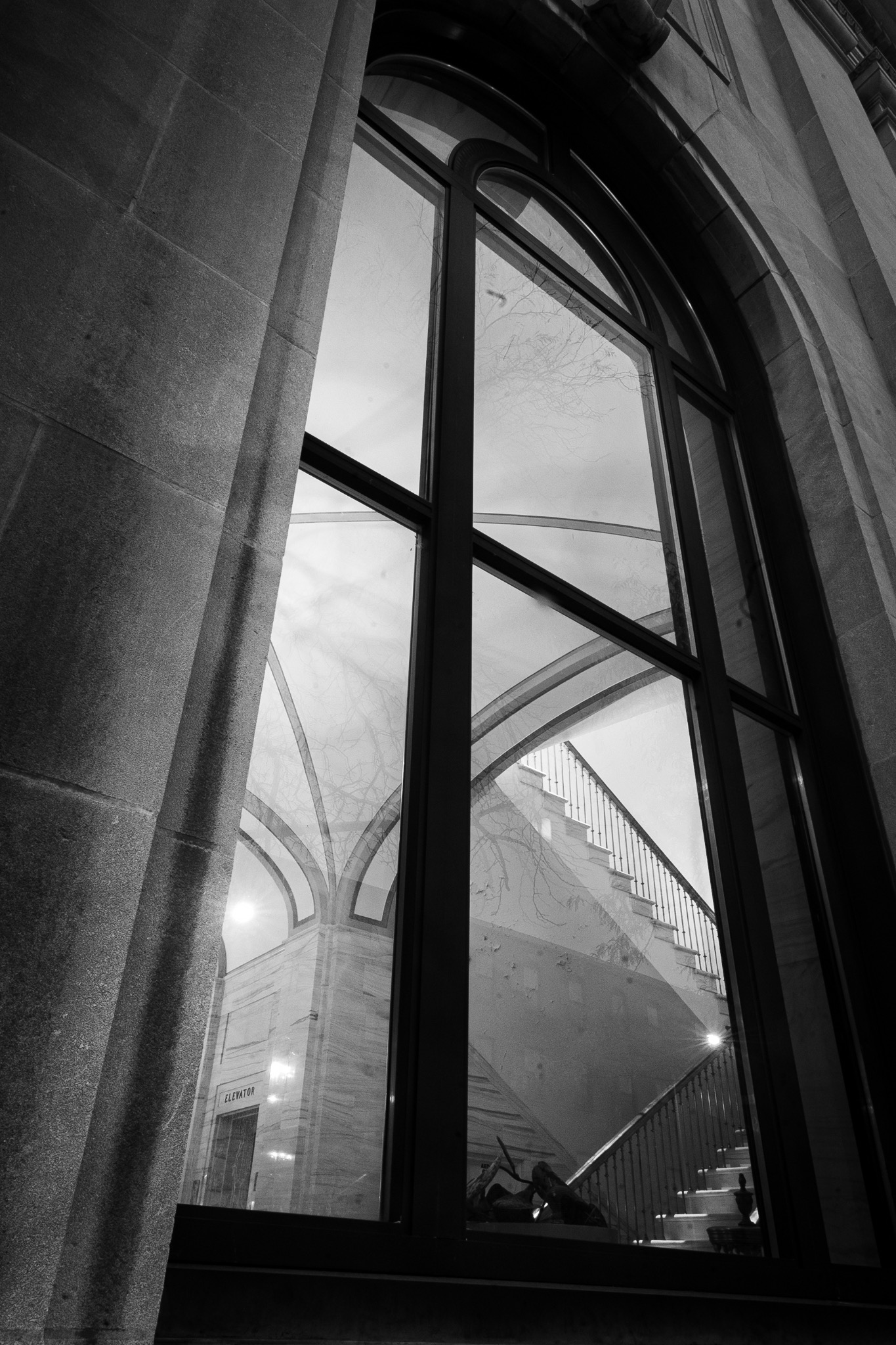 Portrait black-and-white view through an arched window toward interior arches and a staircase